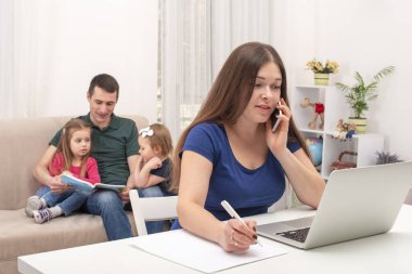Shot of  woman working remotely.  Husband helping the wife, the he is engaged with the children. The modern role of men in the family. clipart