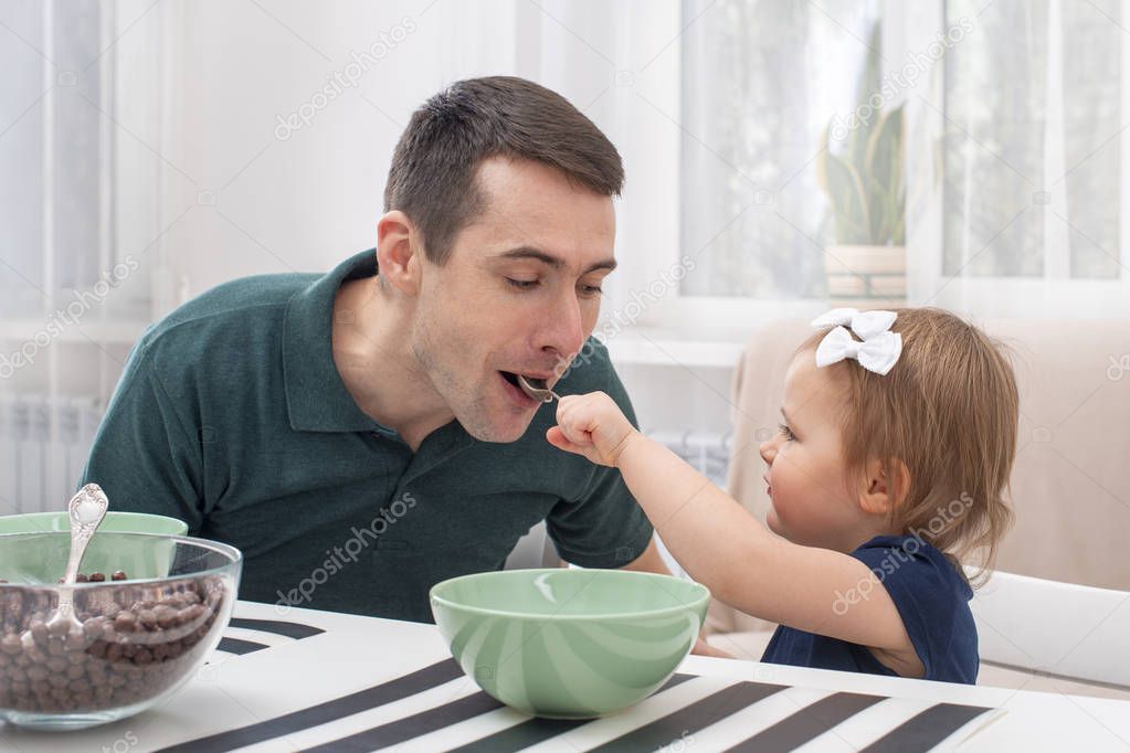 Dad take care of a little daughter at home.  He gave her cereal with milk.  The modern role of men in the family.