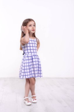 Uzun sarı saçlı genç bir kızın uzun boylu portresi. Stüdyoda beyaz arka planda telefonla konuşuyor.