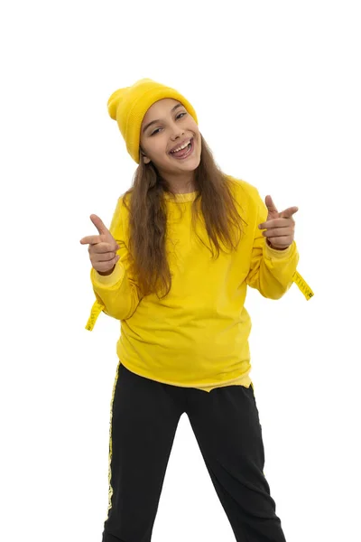 黄色のトラックスーツを着て 白い背景に喜びを表現する手でジェスチャーニット帽を身に着けている若い笑顔の少女ティーンエイジャーの半分の長さの肖像画 幸せな若者のコンセプト — ストック写真