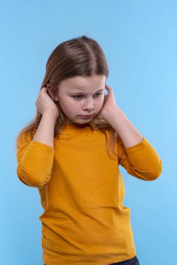 Sarı tişörtlü, uzun saçlı, ciddi sarışın bir kızın yarım boy duygusal portresi. Stüdyodaki mavi arka planla ilgili bir sorun hakkında endişeleniyor.