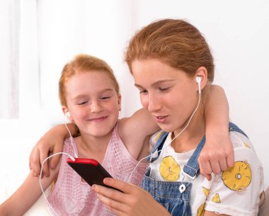 Kızıl saçlı çekici kızların cep telefonu ve kulaklıklarla zaman geçirmesi. Gençlik Yaşam Tarzı Konsepti 