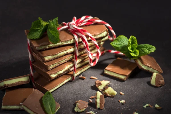 Shot of chocolate with a mint layer tied with a white and red  decorative rope lying on a dark texture table. Fresh mint leaves nearby