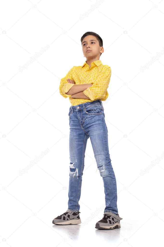 Full length portrait of the serious   boy  of the brunette with arms crossed wearing  yellow shirt and jeans on a white background in studio.