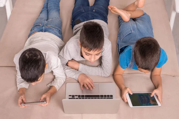 Três Meninos Deitados Sofá Casa Usando Laptop Tablet Smartphone Estilo — Fotografia de Stock