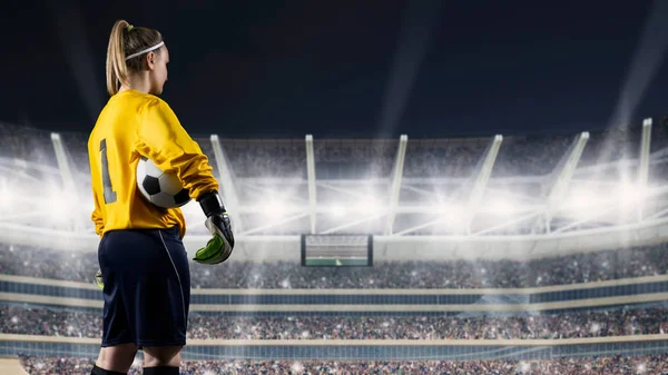 Kobiece bramkarz stoi z piłką przeciw zatłoczonym stadionie w nocy — Zdjęcie stockowe