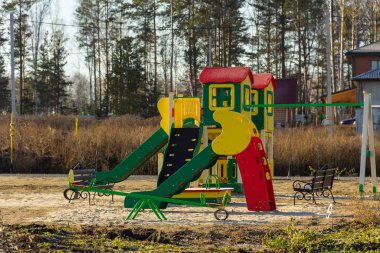 playground in the cottage village under construction in a field overgrown with grass with forest at the background. Autumn, sunny day