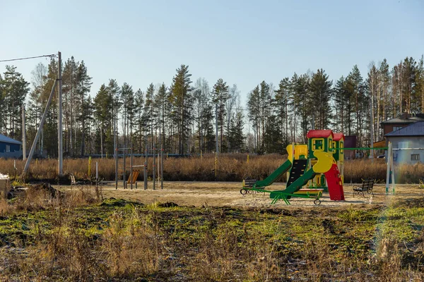 Speeltuin in het huisje dorp in aanbouw in een veld begroeid met gras met bos op de achtergrond. Herfst, zonnige dag — Stockfoto