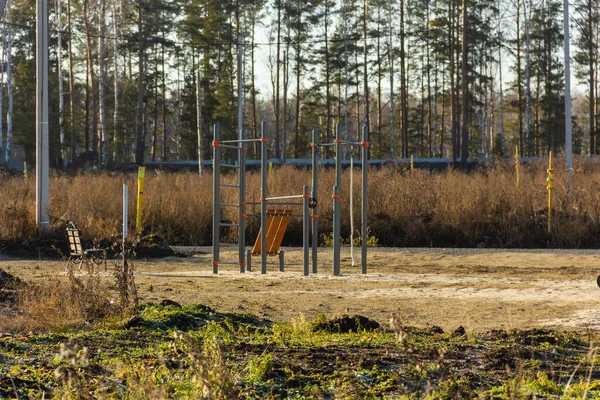 Детская площадка в строящемся коттеджном поселке на заросшем травой поле с лесом на заднем плане. Осень, солнечный день — стоковое фото