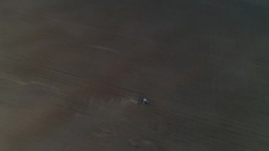 Bir traktör ormanın arka planında büyük bir tarlayı sürüyor. Bahar. Yapraksız ağaçlar. İyi akşamlar.