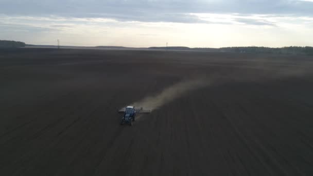 Un tracteur laboure dans un immense champ sur le fond de la forêt. Le printemps. Arbres sans feuilles. Bonsoir. 
