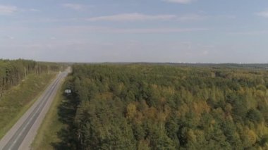 Sonbahar ormanındaki otobanın havadan görünüşü. Otoyol boyunca arabalar ve kamyonlar sürüyor. Gökyüzünde birkaç bulut. Ağaçlar farklı renklerde. Sakin bir sonbahar gününde ormanın havadan görünüşü. Sonbahar orman manzarası