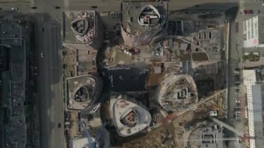 Şehirdeki yüksek binaların ve vinçlerin havadan çekilmiş görüntüleri. Kentsel altyapı geliştirme. Arabalar sokaklarda geziyor. Yaz güneşli bir gün. Kamera aşağı bakar ve düşer.
