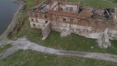 Göletin kıyısındaki tuğla boruyla eski tuğla binanın havadan görünüşü mahvoldu. Köyün yakınlarında. Bahar, bulutlu. Rusya, Chebyabinsk bölgesi, Kaslinsky bölgesi, Vozdvizhenka köyü