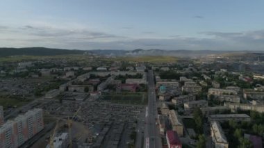 Şehir havadan görülebiliyor. Yüksek ve alçak binalar var. Arabalar sürüyor. Çerçeveli garajlarda, stadyumda, okulda. Arka planda Ural dağları ve bitkiler var. Duman bacalardan geliyor. Yaz, akşam. Rusya, Chelyabinsk bölgesi, Satka şehri
