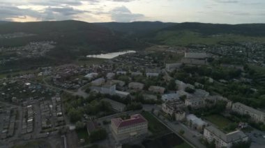 - 10. Düşük binalı şehrin havadan görünüşü. Arabalar sürüyor. Çerçeve garajlarında, okulda, gölde. Arka planda Ural Dağları var. Yaz, akşam. Rusya, Chelyabinsk bölgesi, Satka şehri