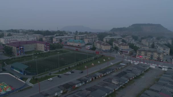 低住宅と夜の街の空中ビュー 市内のスモッグで 車は道路を走る 学校の近くのスタジアムでは 人々はサッカーをする 市内の産業廃棄物の外 ロシア チェリャビンスク地方 サトカ市 — ストック動画