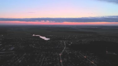 Köyde günbatımının havadan görüntüsü. Arabalar yol boyunca gidiyor. Orman ve tarlaların olduğu köyün etrafında. Yaz, alacakaranlık