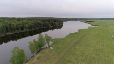 Donanımlı balıkçı iskeleleri olan küçük göl manzarası. Günaydın, bulutlu. Bazı yerlerde, balıkçılar ve çadırları olan arabaları. Gölün bir tarafında orman, diğer tarafında çimen var..