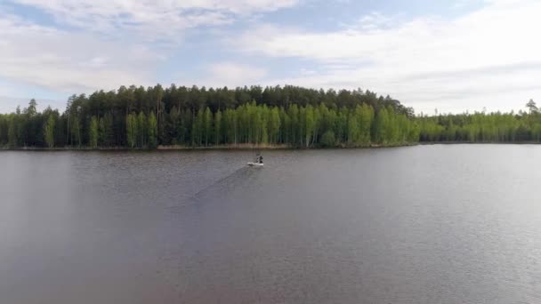 森に囲まれた湖の空中ビュー ゴム製の膨脹可能なボート釣りの2人の漁師 釣り竿で立っている魚屋さんもいます 晴れた夏の日 — ストック動画