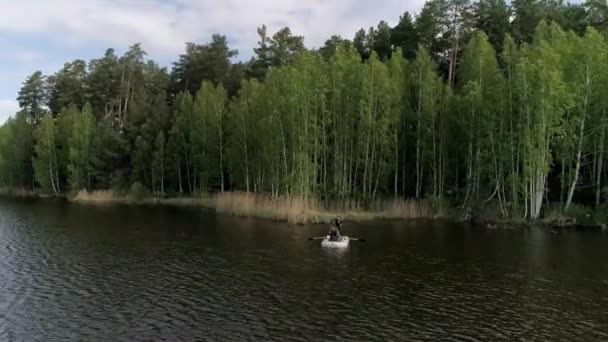 环绕着森林的湖景 两名渔民在一条橡皮艇上钓鱼 一个渔夫划船 另一个拿着钓竿 阳光灿烂的夏日 — 图库视频影像