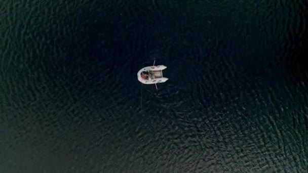ゴム製のインフレータブルボート釣りで2人の漁師と湖の空中ビューをトップダウン 釣り竿を持った魚の漕ぎ耳がひとつ 晴れた夏の日 — ストック動画