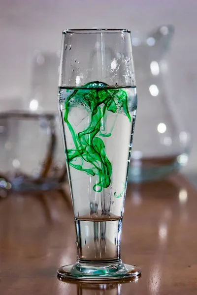 Close up of green ink in water glass on table — Stock Photo, Image