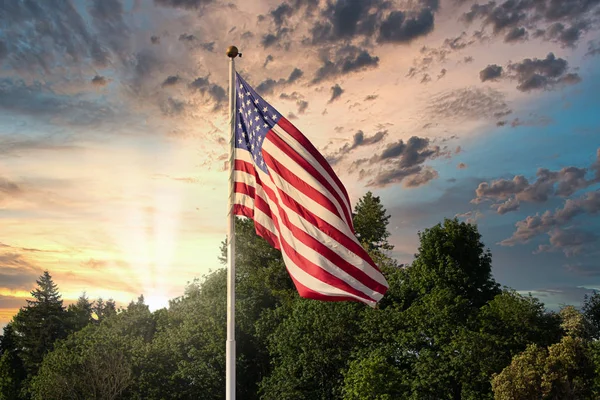 Por do sol e tempo com céu nublado atrás da bandeira americana soprando no vento — Fotografia de Stock