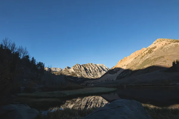 dark shadowed lake along bright muntain peaks