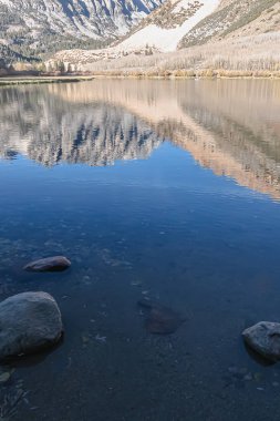 Parlak mavi su, sabah parlayan dağları yansıtır.