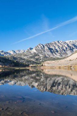 Parlak mavi su, sabah parlayan dağları yansıtır.