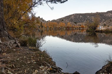 Büyük göl sonbahar ağaçlarının renklerini ve dağı yansıtıyor.