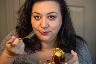 Uzun siyah bukleli güzel kadın pasta yiyor.