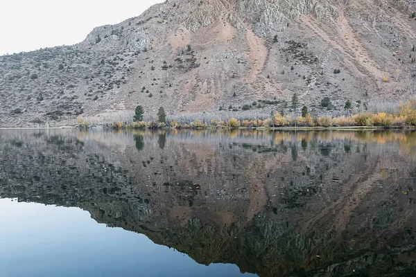 Lago de montanha reflexivo com pinheiros aspens grama e montanha — Fotografia de Stock