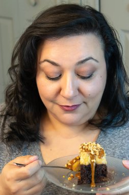 Olgun bir kadın mutfakta çikolatalı pasta yiyor.