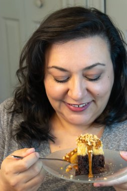 Olgun bir kadın mutfakta çikolatalı pasta yiyor.