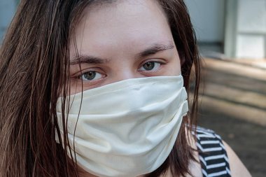 Korunmak için maske takmış koyu renk saçlı genç bir kadın.