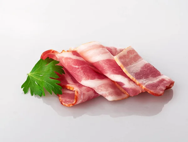 bacon in slices and rolls with a sprig of fresh red Basil isolated on a white background