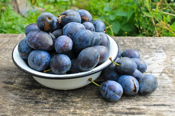 Fresh plums in rustic bowl on old wooden background — Stock Photo, Image