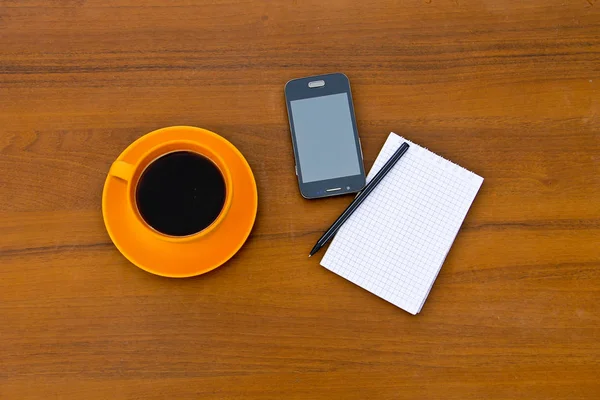Tazza da caffè con smartphone, blocco note e penna su scrivania in legno — Foto Stock