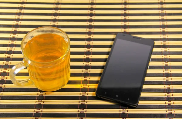 Smartphone negro y taza de té en estera de bambú —  Fotos de Stock