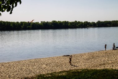 Küçük çocuk nehir kıyısındaki kumsalda uçurtma fırlatıyor.
