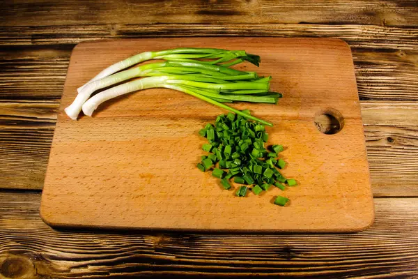 Chopped green onions on cutting board on wooden table — Stock Photo, Image