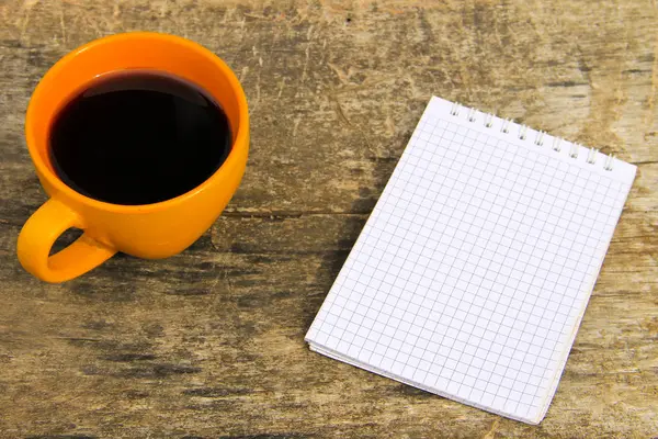 Tasse Kaffee mit leerem Notizblock auf Holztisch — Stockfoto