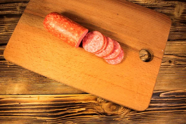 Sausage sliced on cutting board on wooden table — Stock Photo, Image
