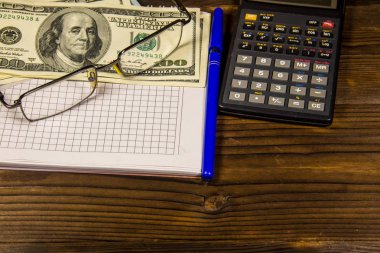 Defter ile dolar, kalem, gözlük ve ahşap masa hesap makinesi