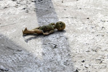 Gri beton zeminde terk edilmiş kırık bir oyuncak bebek.