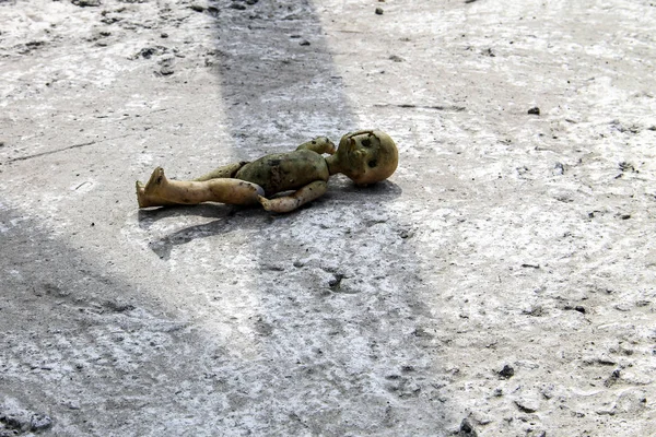 Gri beton zeminde terk edilmiş kırık bir oyuncak bebek.