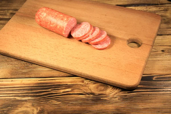 Sausage sliced on cutting board on wooden table — Stock Photo, Image