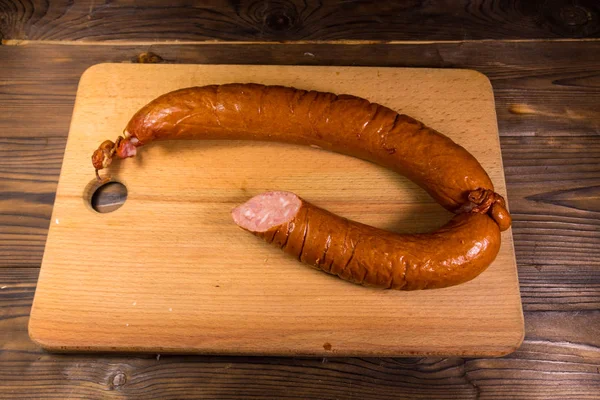 Smoked sausage on cutting board on wooden table — Stock Photo, Image